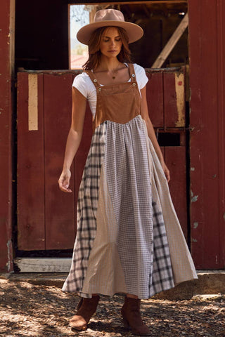 Woman wearing a brown apron over a white shirt and plaid skirt, standing in front of a red wooden door.