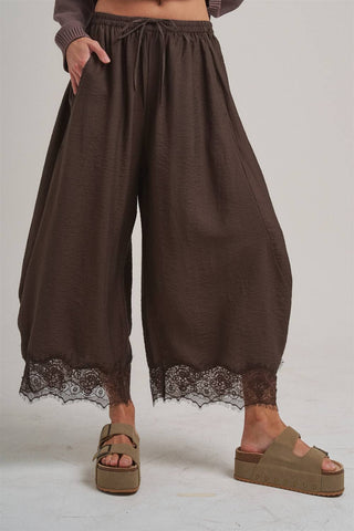 Brown wide-leg pants with lace trim worn by a person on a white background