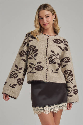 Woman wearing a beige cardigan with black floral patterns on a plain background