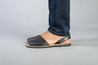 Person wearing black sandals with a visible brand logo on a gray background