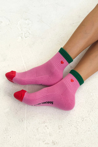 Pink socks with red toes and green cuffs worn by a person on a light background