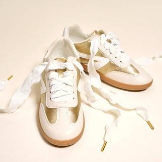 Pair of white sneakers with brown soles on a light beige background
