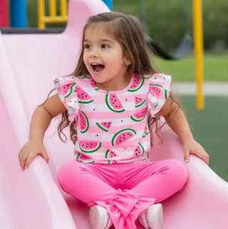 Child sliding down a pink slide wearing a watermelon-patterned shirt and pink pants.