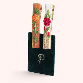 Two decorative hair clips with floral designs on a black pouch against a white background