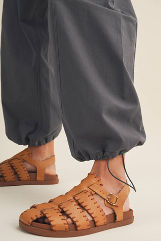 Brown woven sandals worn with gray pants on a light background