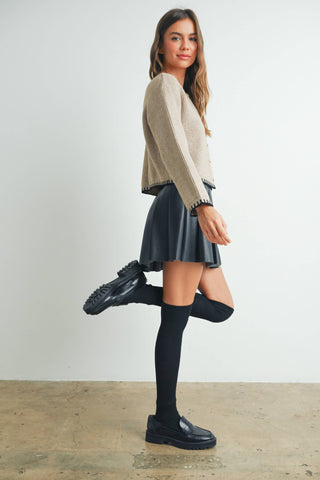 Woman wearing a beige sweater, black skirt, and black shoes on a plain background