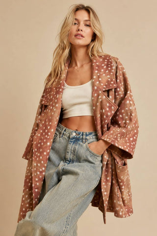 A woman models a brown open-front cardigan with a white polka dot pattern, worn over a white crop top and light-wash blue jeans, set against a solid beige background.