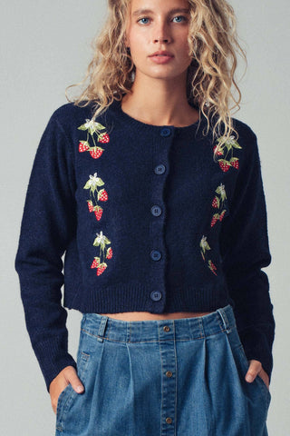 Woman wearing a navy blue cardigan with floral embroidery on a plain background