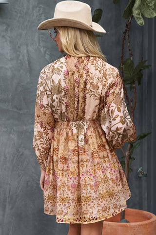 Person wearing a floral dress with a wide-brimmed hat against a gray wall.