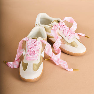 White sneakers with pink checkered laces on a beige background