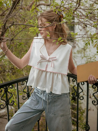 Woman wearing a white blouse with pink trim and light blue pants, standing outdoors.