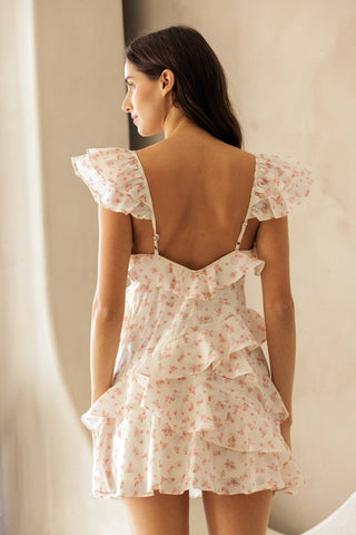 Woman wearing a floral dress with a backless design, standing against a neutral background.