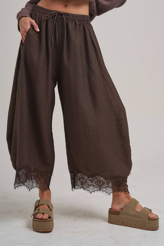 Brown wide-leg pants with lace trim worn by a person on a plain background