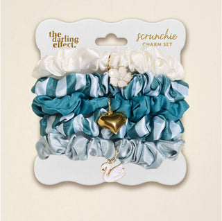 Set of scrunchies with charms on a branded card, displayed against a beige background.