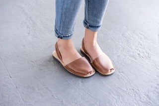 Brown sandals worn with rolled-up jeans on a light gray floor.