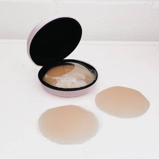 Two silicone adhesive pads and an open container on a white background