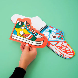 Colorful paper shoes held by a hand on a green background