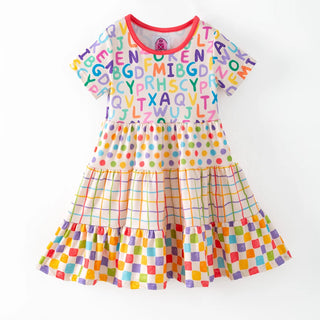 A short-sleeve tiered baby dress with a colorful alphabet print on the bodice, polka dots, and plaid and checkered patterns on the skirt, shown on a plain white background.