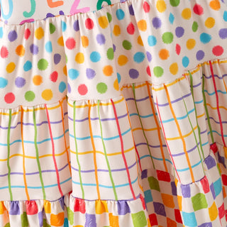 Close-up of a ruffled skirt fabric with a multicolor polka dot pattern on the upper section and a multicolor plaid pattern on the lower tiers, on an off-white background.