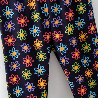 Close-up of a pair of leggings with a colorful daisy pattern on a dark navy background, photographed against a light neutral backdrop.