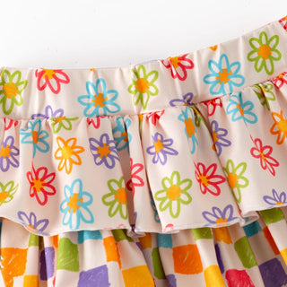 Close-up of a ruffled skirt with a colorful floral print on a cream background, featuring layered ruffles and a checkered patterned section below.