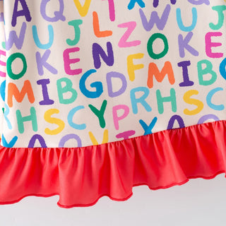 Close-up of a children's dress or skirt featuring colorful alphabet letters printed across an off-white fabric, with a bright red ruffled hem.