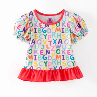 A girls' short-sleeve top with an all-over colorful alphabet print on a white base, featuring a bright red ruffled hem and red trim on the neckline and sleeves, shown against a plain white background.