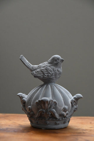 Decorative bird sculpture on a pedestal against a gray background