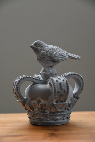 Decorative object resembling a crown with a bird on top, placed on a wooden surface.