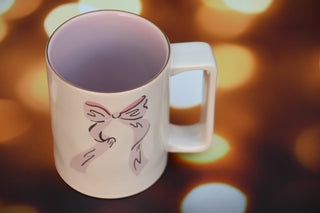 Ceramic mug with pink bow and gold detail.