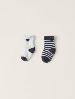 Two pairs of baby socks, one white with black patterns and the other gray with black and white stripes, on a beige background.
