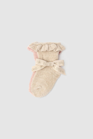 Beige baby sock with ruffle and bow detail on a light pink background
