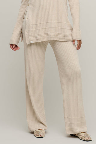 Person wearing a beige ribbed suit with wide-leg pants on a plain background