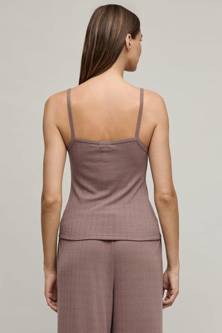 Woman wearing a brown ribbed tank top and pants on a plain background