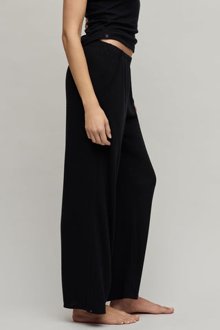 Person wearing black wide-leg pants and a black top on a plain background