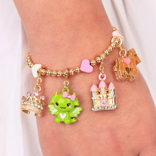 A close-up of a gold charm bracelet worn on a wrist, featuring a green dragon, pink castle, gold crown, and pink heart charms.