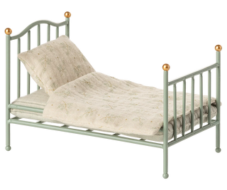 Small green metal bed with beige bedding on a white background