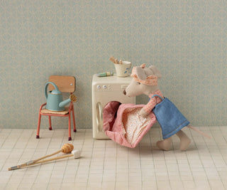 Miniature scene with a toy mouse, chair, and washing machine against a patterned wall.