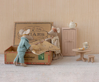 Two toy mice in a room with a suitcase, table, and cabinet.