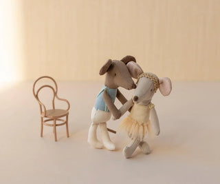 Two toy mice in ballet costumes standing next to a small chair on a light background