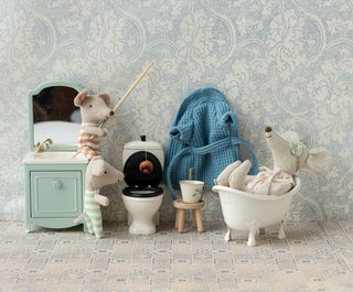 Miniature bathroom set with toy animals and furniture against a patterned wall.