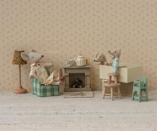 Miniature diorama with toy mice and furniture against a floral wallpapered wall.