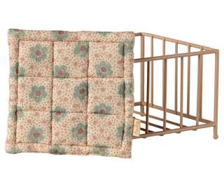 Floral-patterned quilt draped over a baby crib on a white background