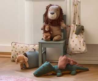 Plush toys including a lion, teddy bear, and dinosaur on a chair and floor.