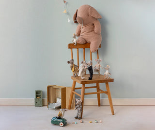 Children's toys including a plush elephant and teddy bears on a wooden stool against a light blue wall.