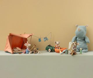 Set of toy animals with a tent and car on a light green surface against a beige wall.