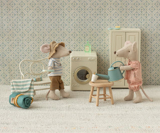 Two toy mice in a miniature room with a washing machine and other items.