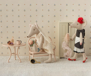 Two plush toys, one resembling a mouse and the other a cat, in a room with floral wallpaper.