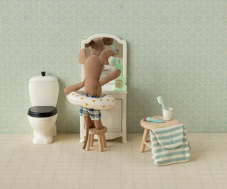 Stuffed teddy bear in a bathtub with bathroom items and wallpaper.