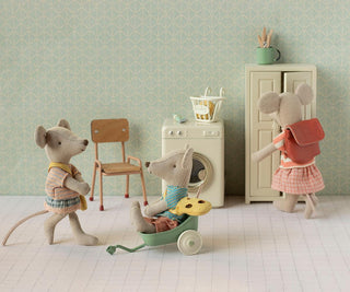 Three toy mice in a room with a chair, washing machine, and cabinet.